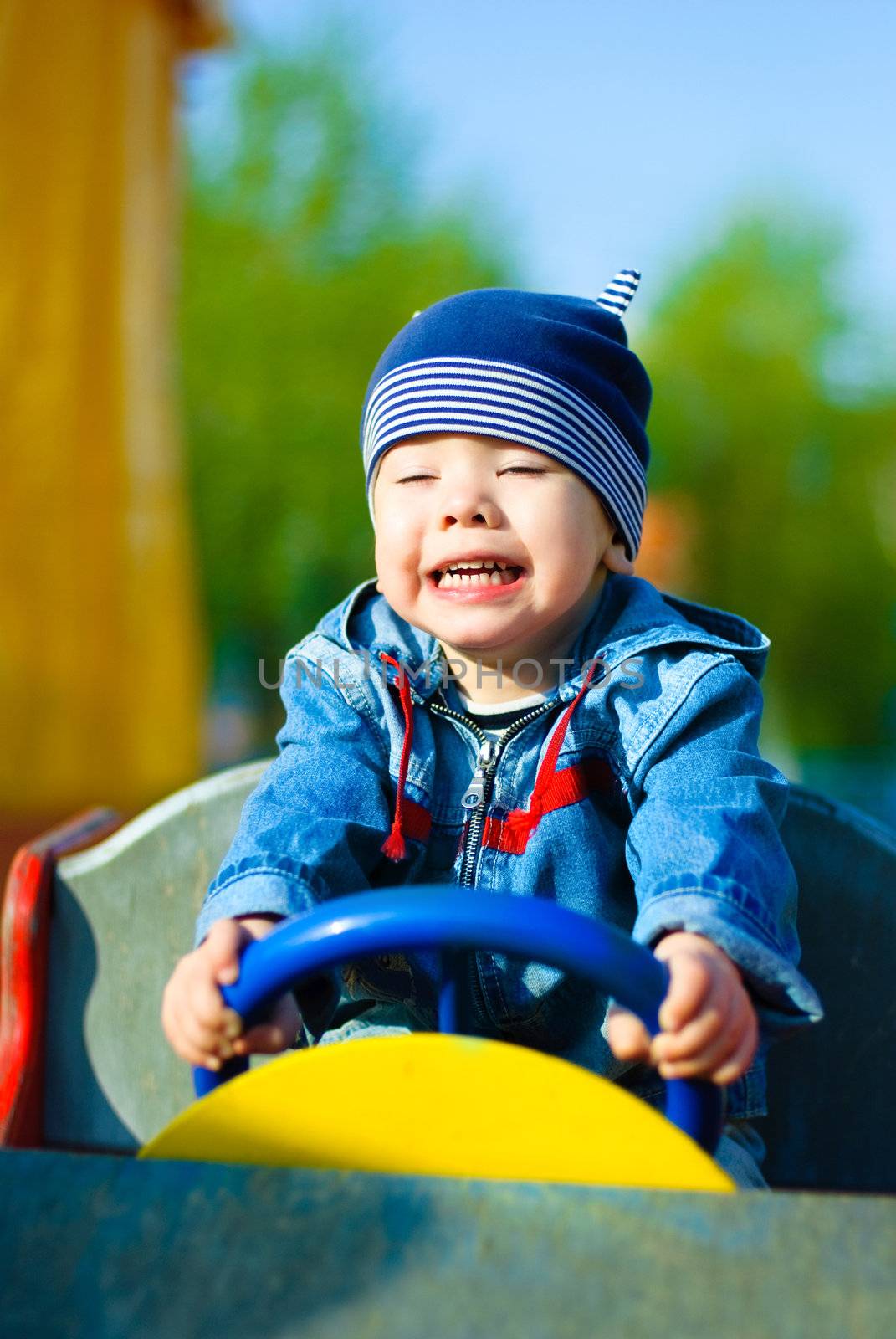 happy three year old boy driving a toy car outdoor in the park