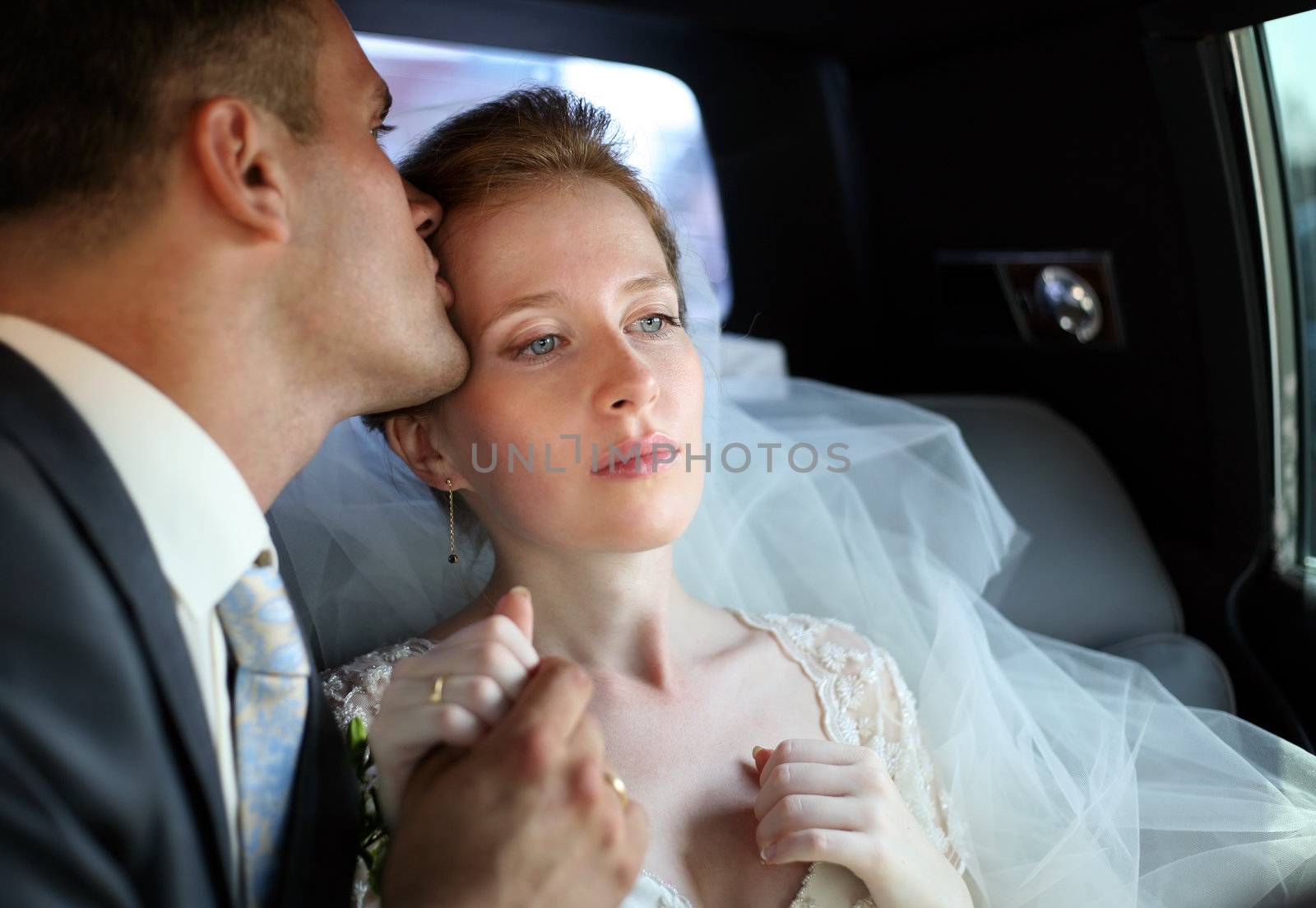 The groom kisses the bride in the automobile