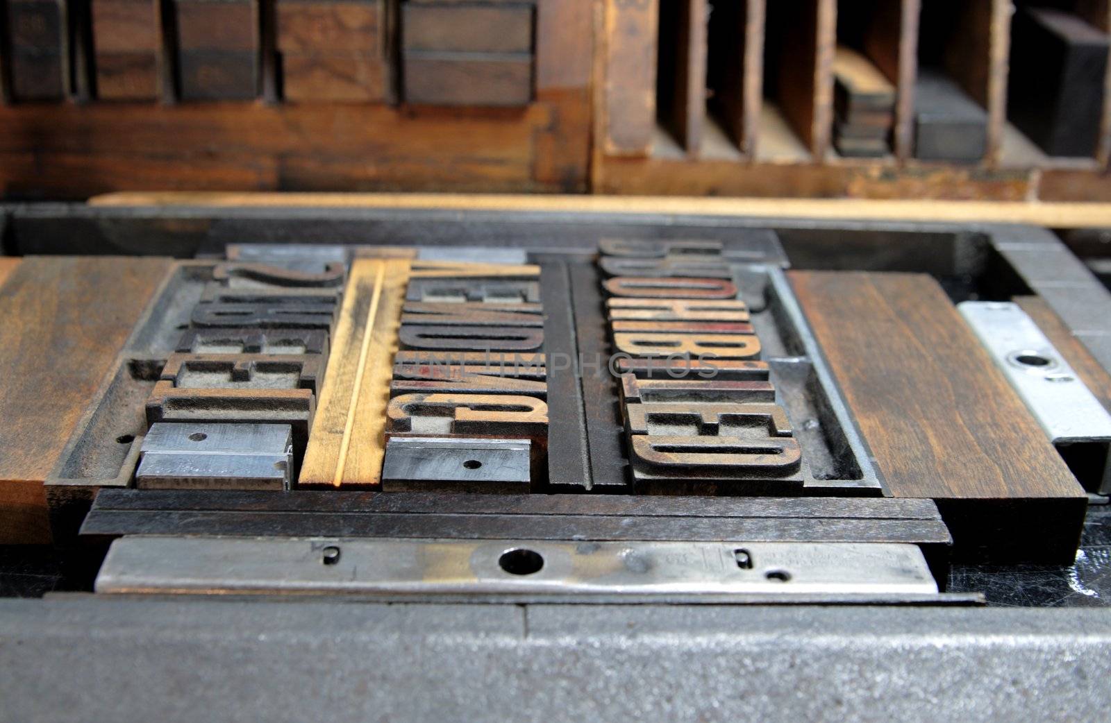 wood type clamped into a printer's chase just before inking, against a background of printer's furniture
