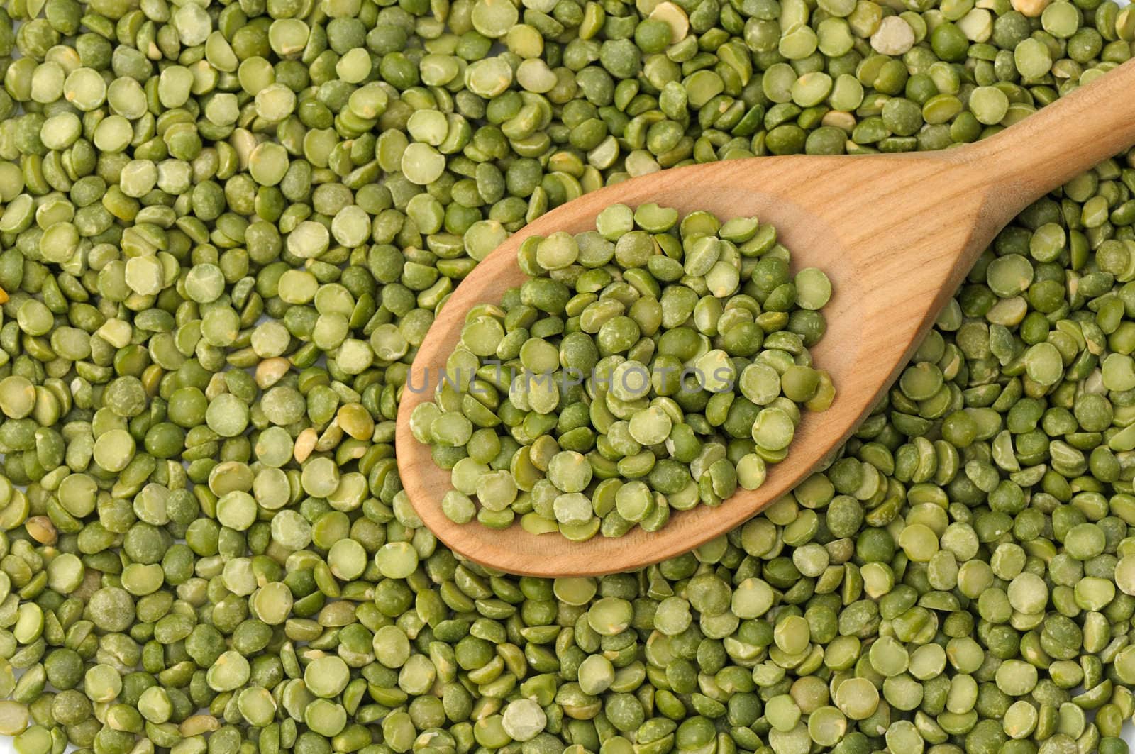 Wooden spoon full of split green peas on legume background