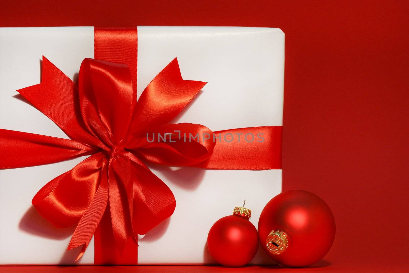 Big red bow on gift with red background and christmas balls