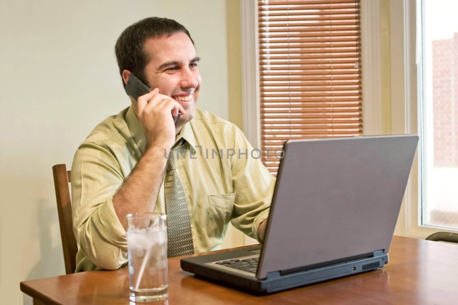 A happy man working from home with his cell phone and laptop.