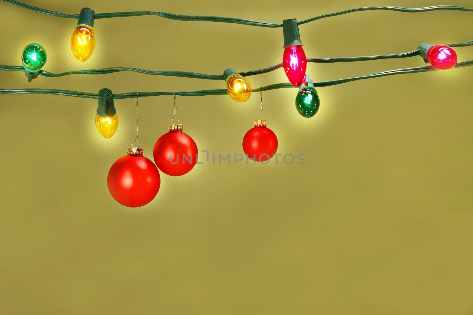 Three red christmas balls hanging on a set of colored tree lights