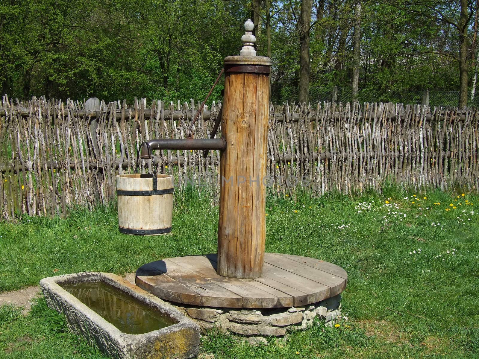 Old wooden pump in village, green grass around