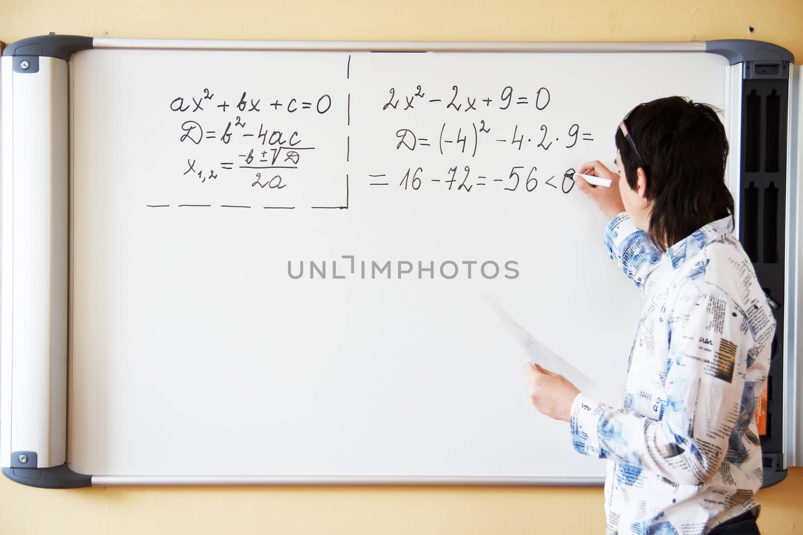 Young teacher teaching algerbra  and writes quadratic equation on a whiteboard