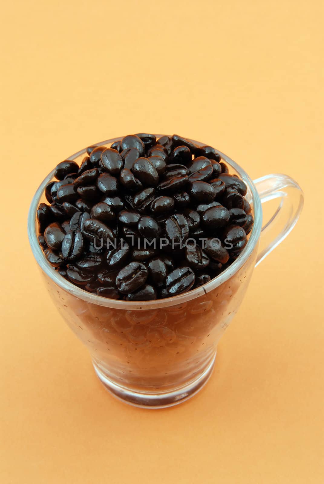 Transparent glass full with coffe beans isolated on orange background