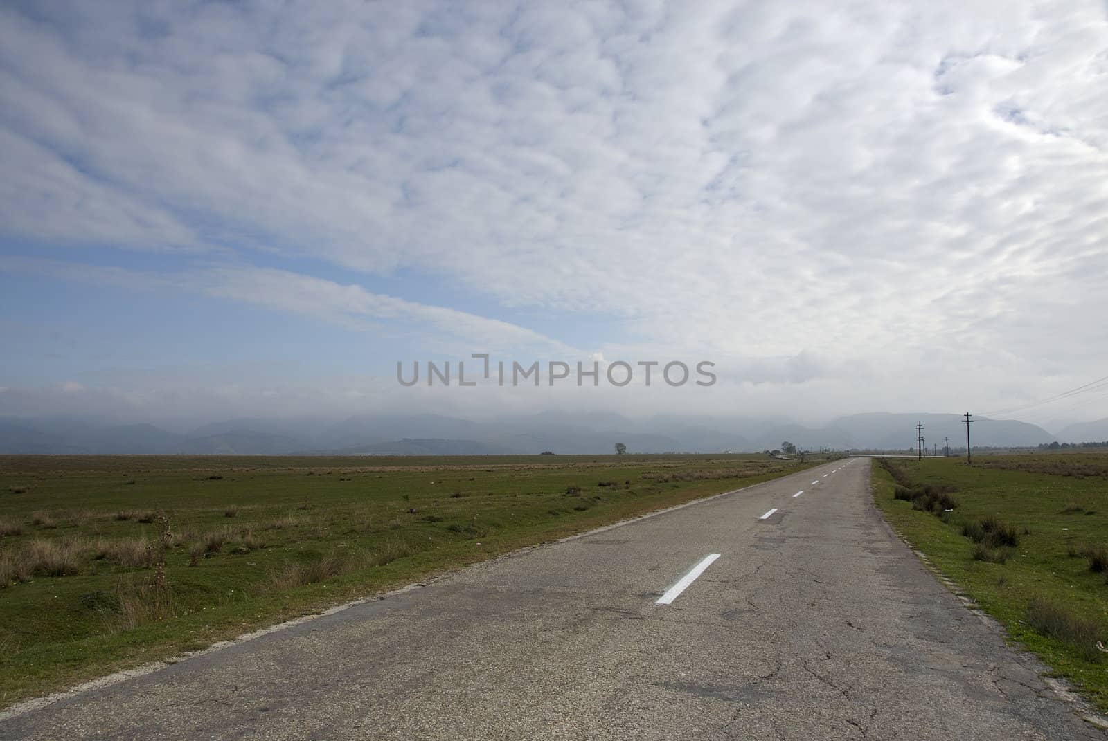 Sunny rural landscape with long straight road and blue cloudy sky