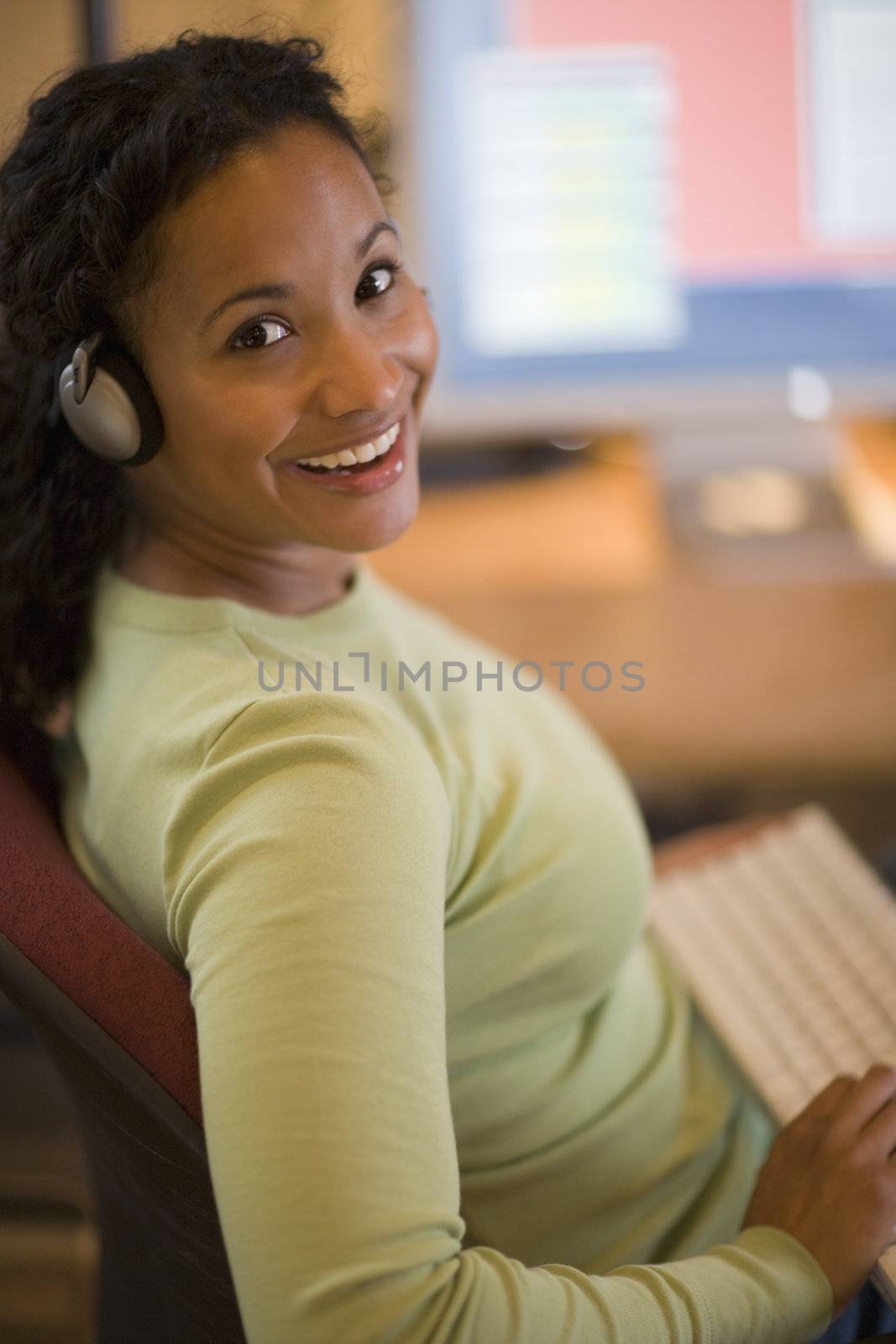 Smiling young African American woman with keyboard in lap and computer on desk