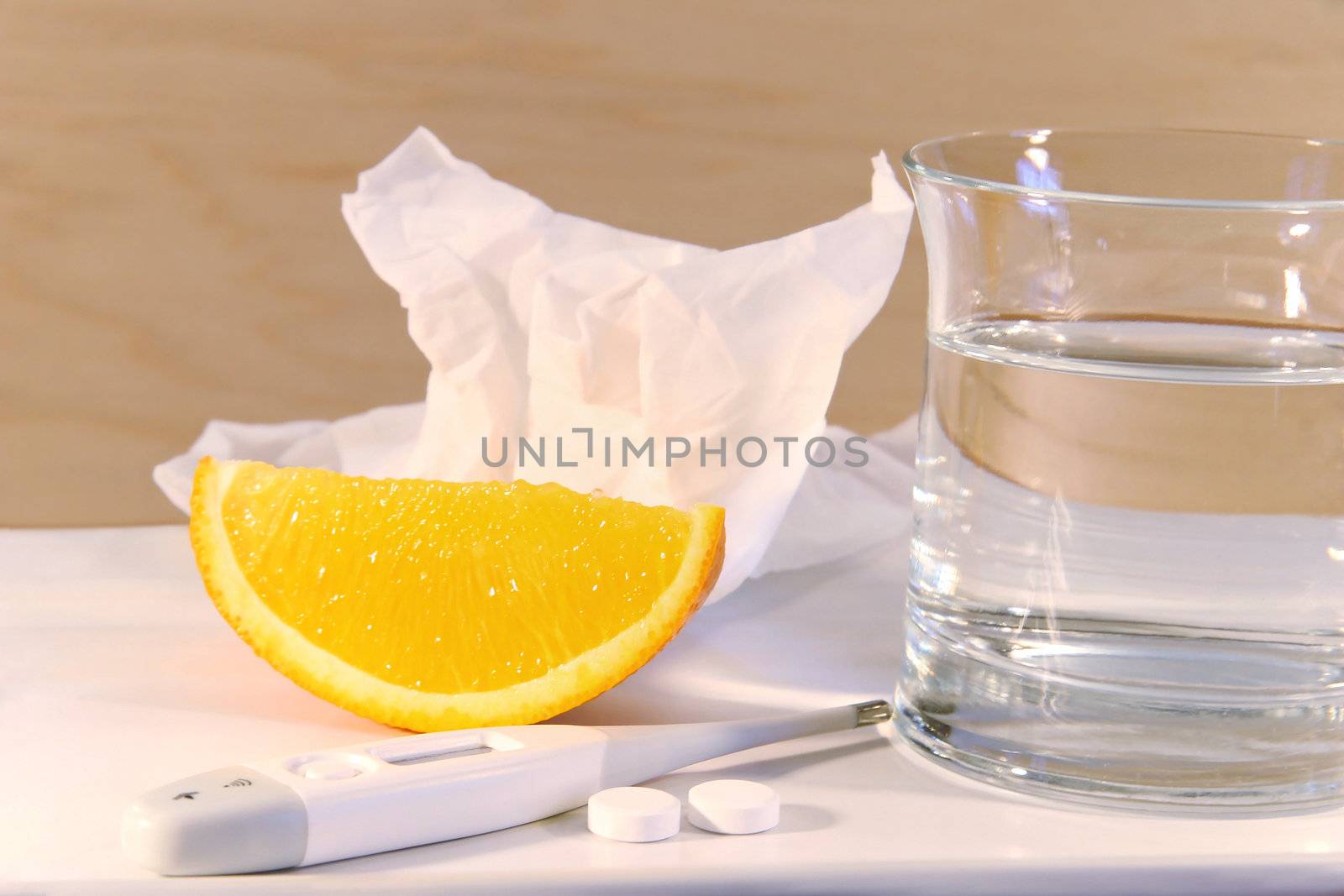 Water glass with cold pills,tissue, thermometer and orange to fight flu symptoms