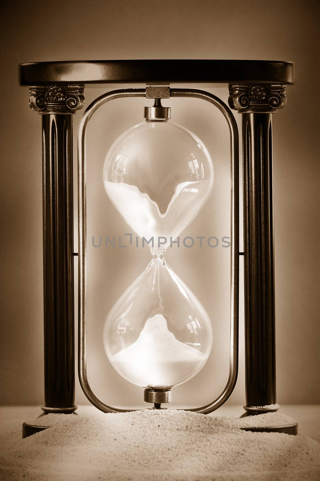 Hourglass resting on beach sand showing sand falling through glass