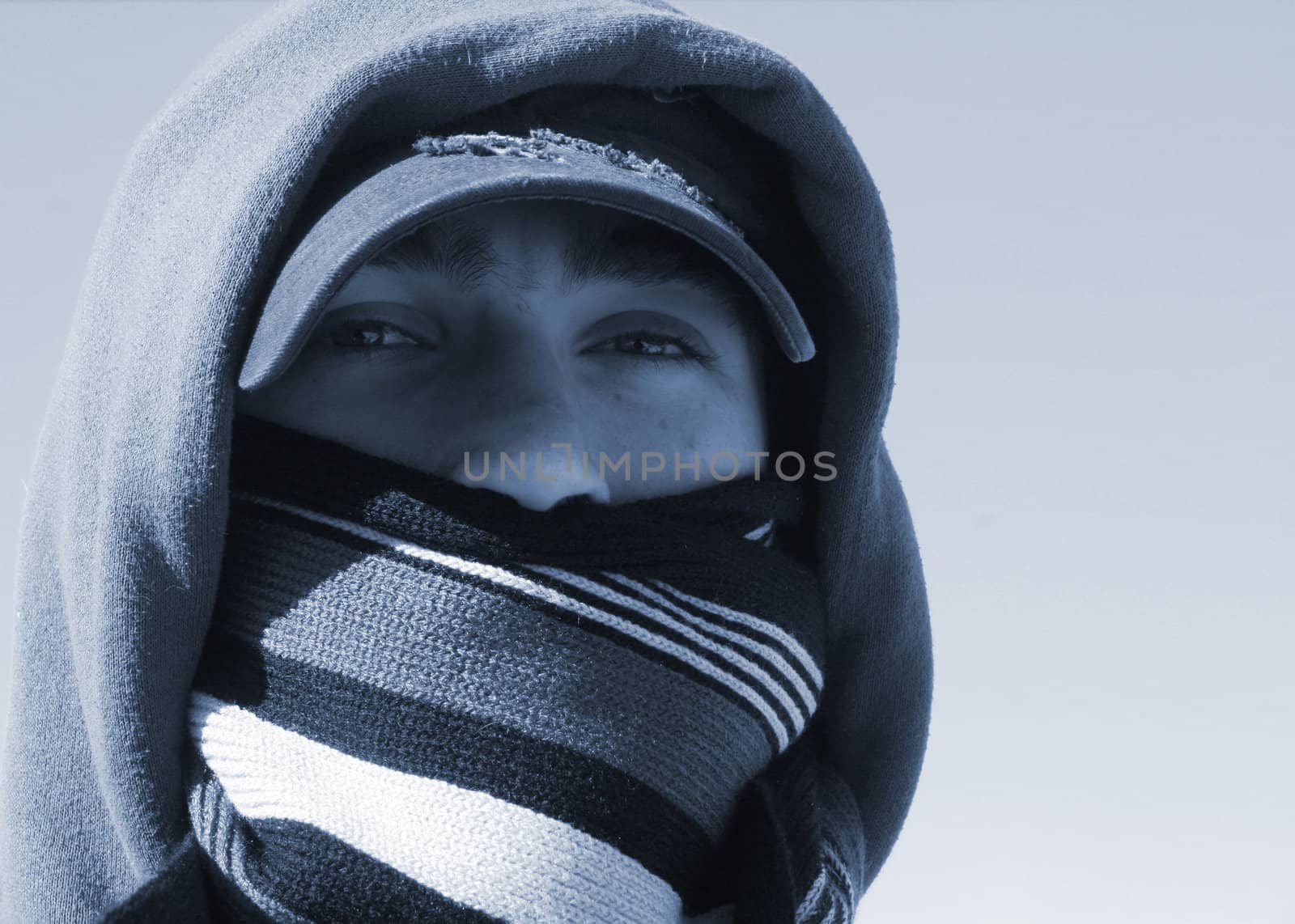 Duo-toned image of handsome young man with hat and knitted wool scarf covering his mouth on a cold winter day.