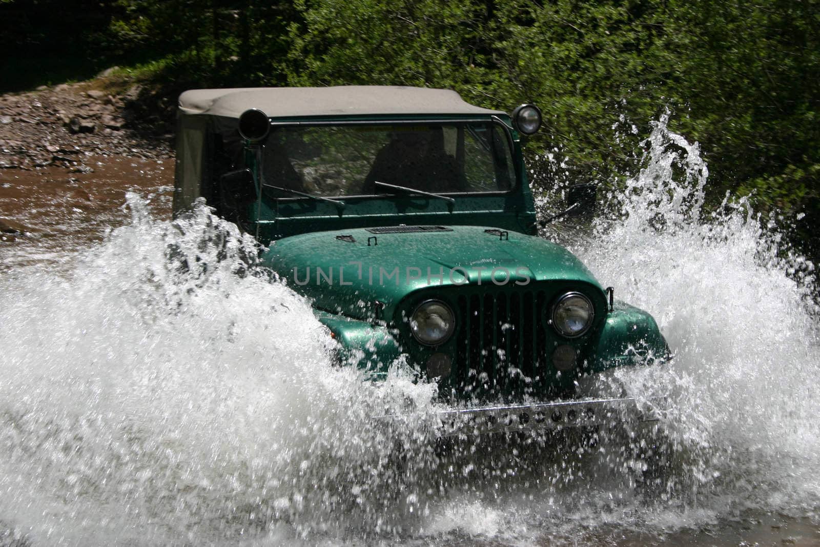 Popular four-wheel-drive vehicle plows through mountain stream creating large spray of water