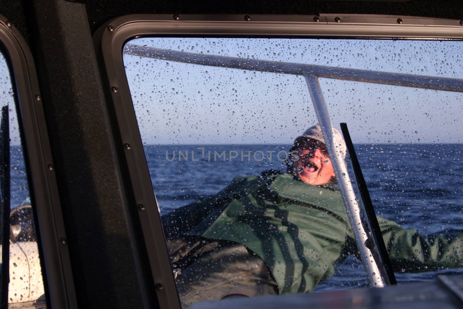 Deck hand on small fishing boat appears to be falling overboard as we look through a spray-spotted window