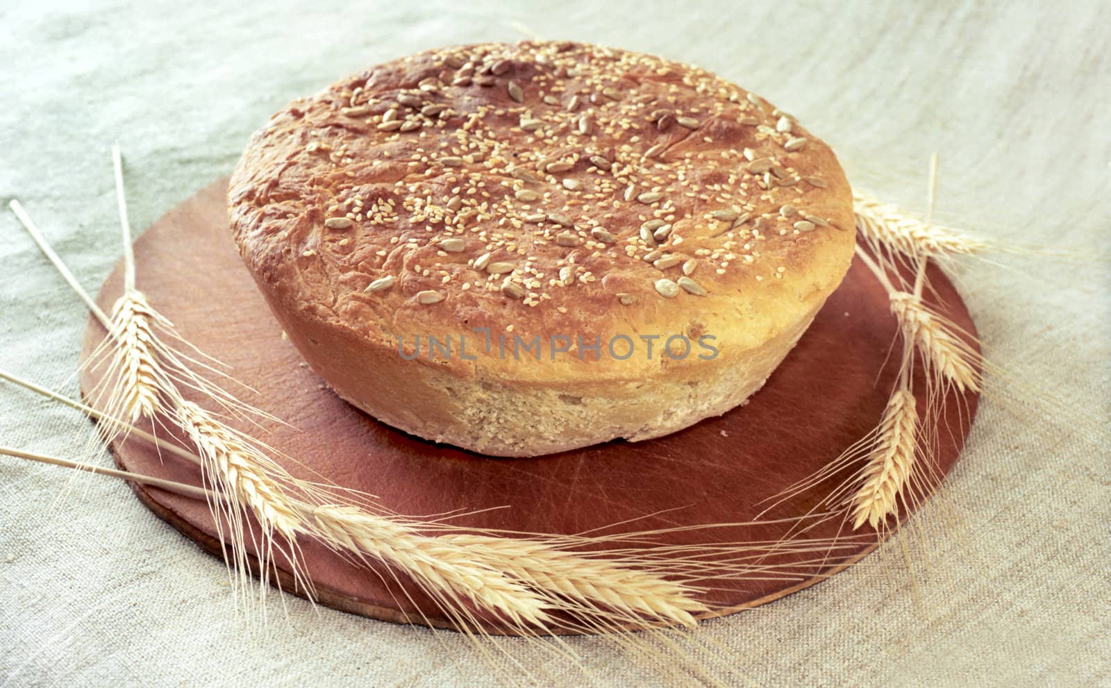 Round loaf of rye bread with spikes on wooden breadboard