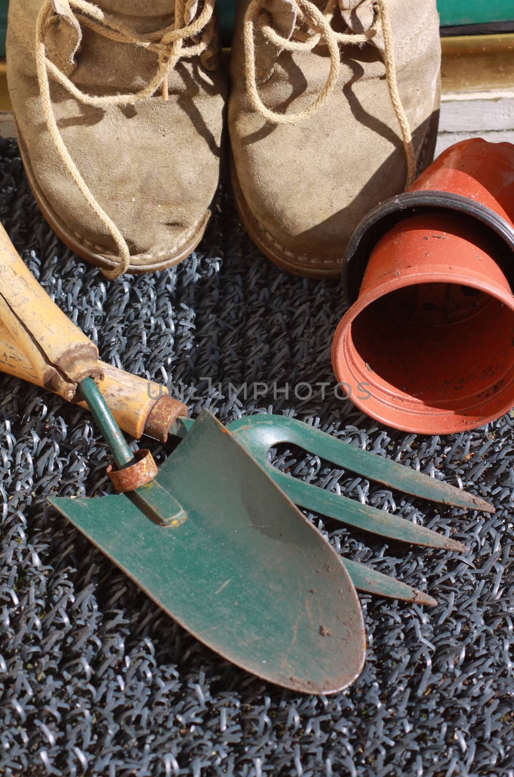 A pair of gardening boots with terracotta coloured pots and gardening tools.