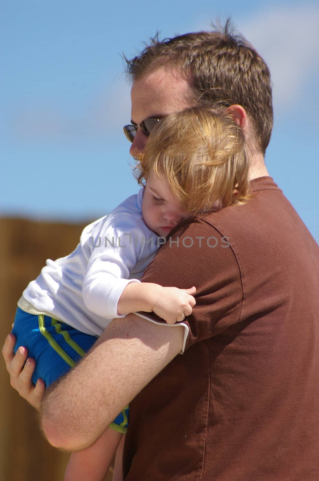 A young father and daughter are sharing a hug outside in the sun