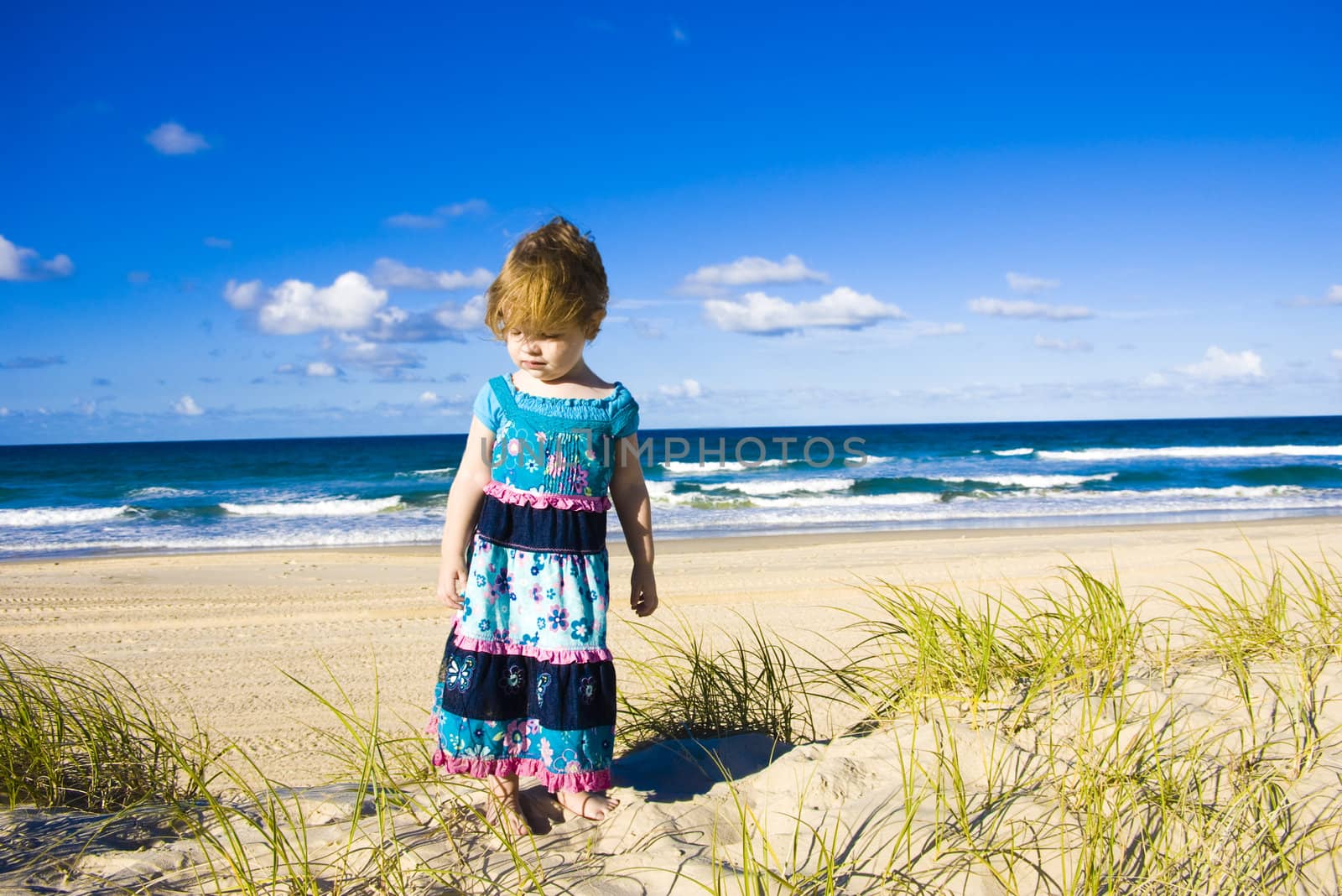 A young girl is wandering around on sand dunes at a beach during a sunny day