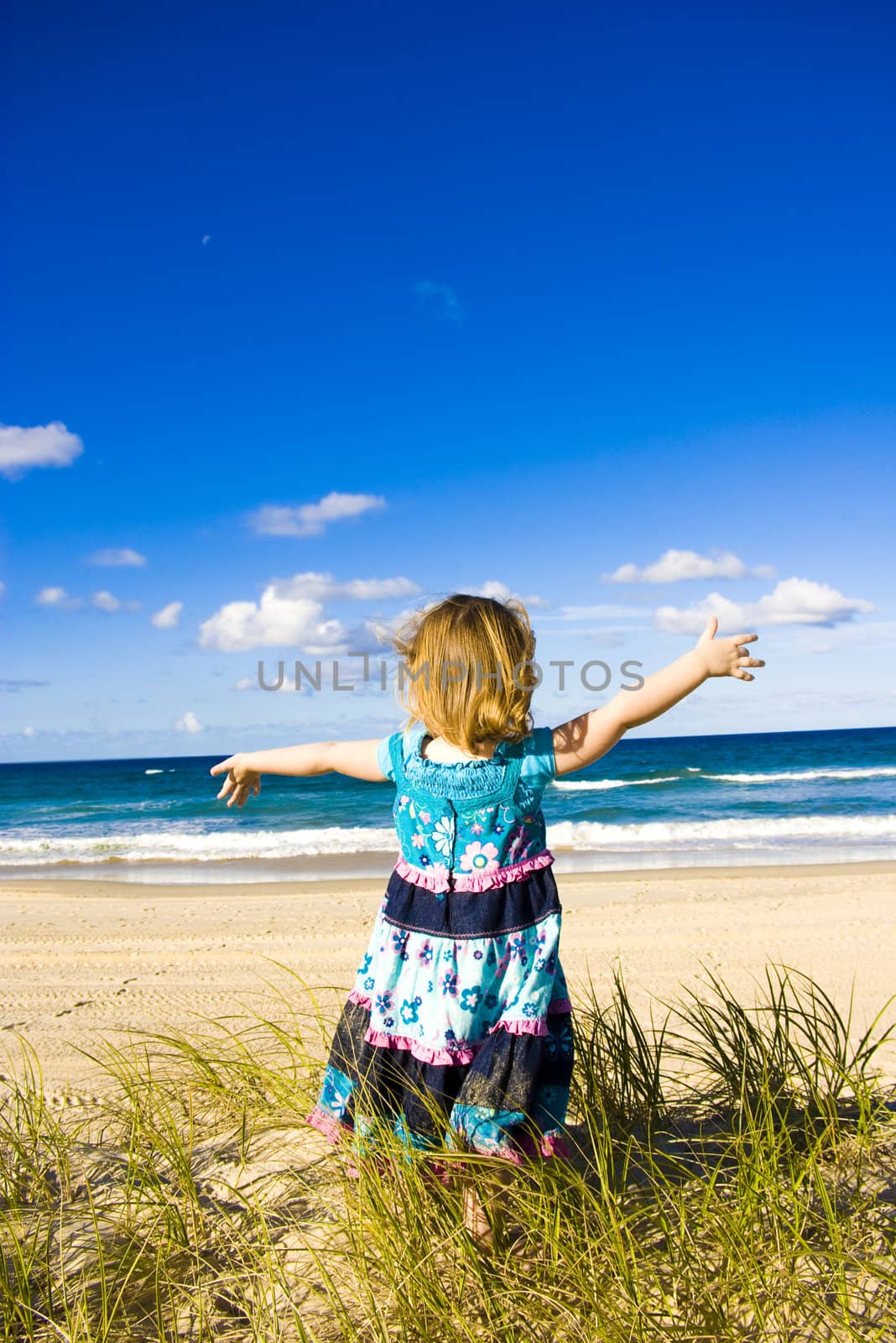 A pretty little girl standing a sand dune on the beach with her arms stretched out