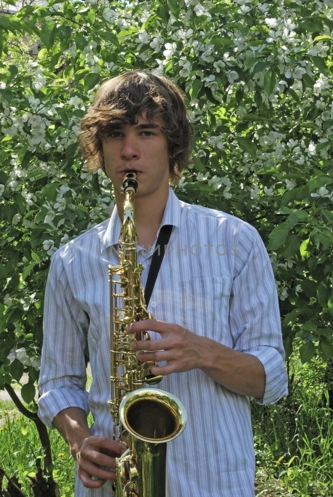 the young man with saxophone on the background of the flowering tree