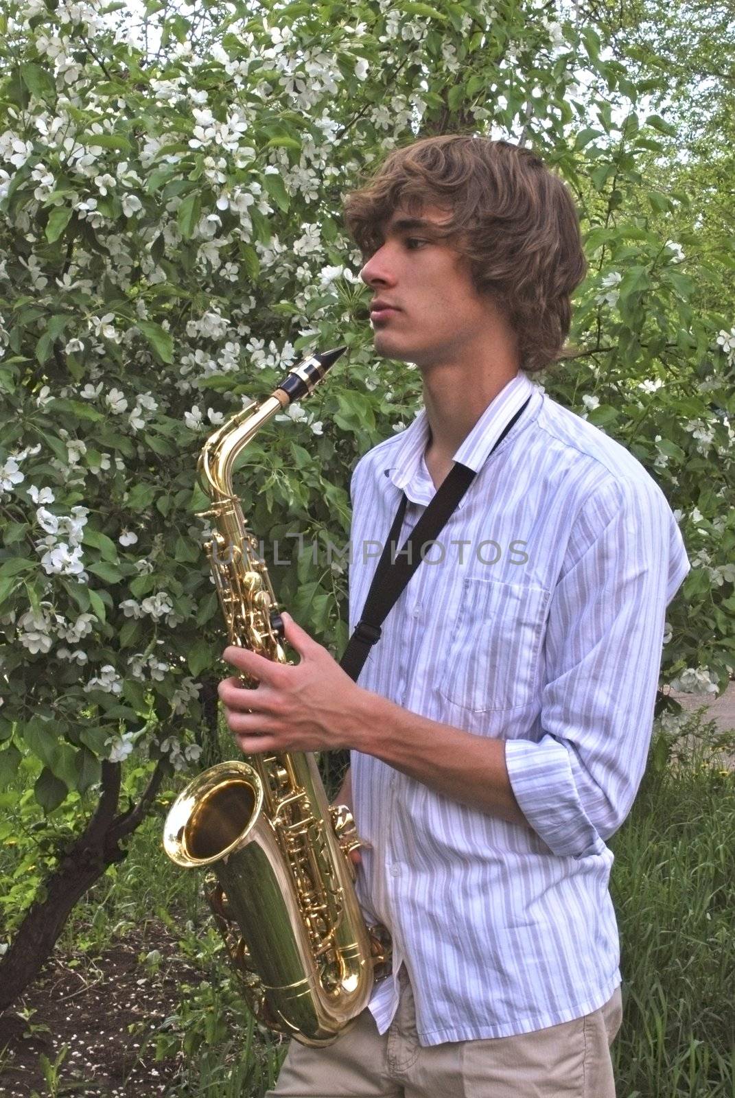 the young man with saxophone on the background of the flowering tree