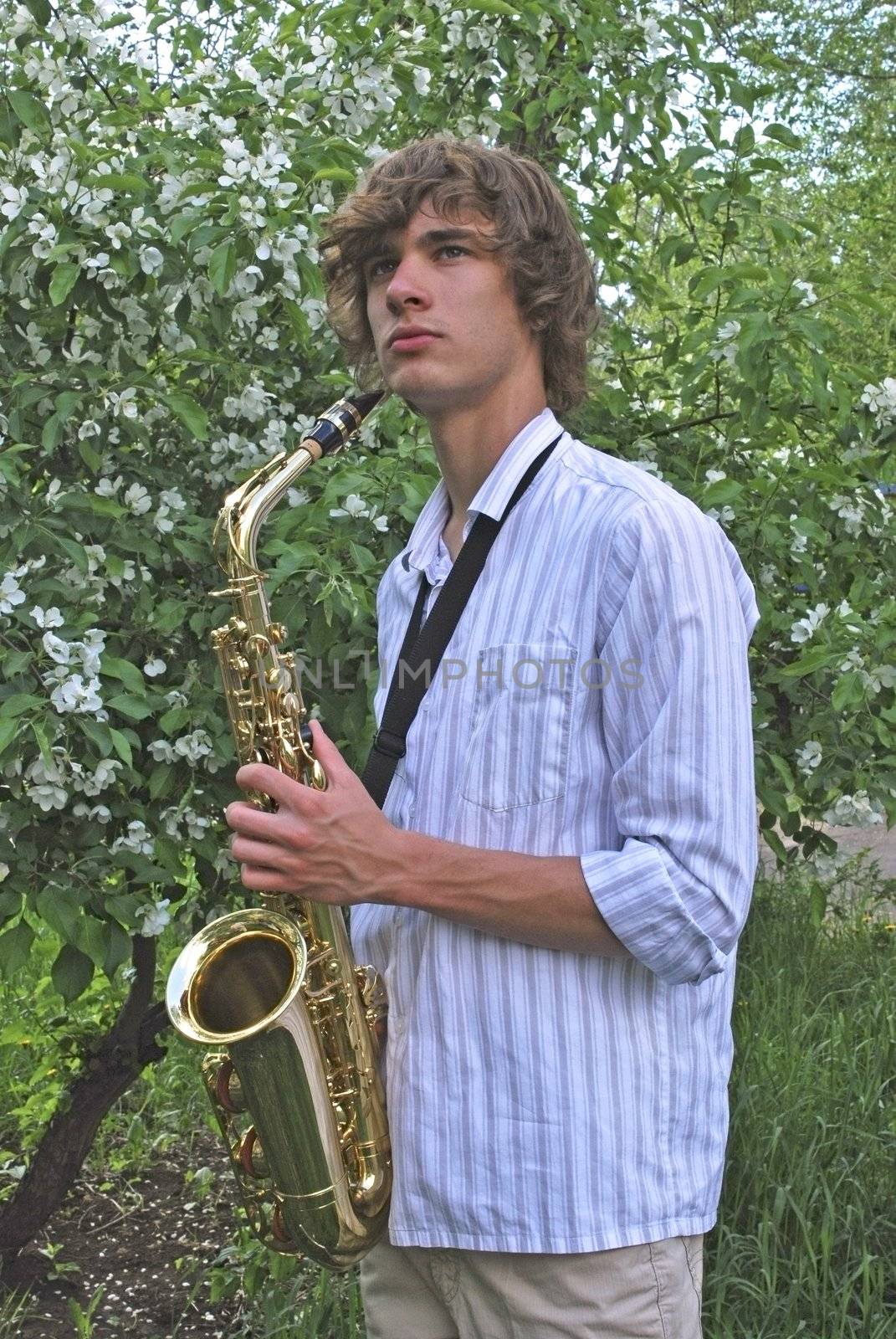 the young man with saxophone on the background of the flowering tree