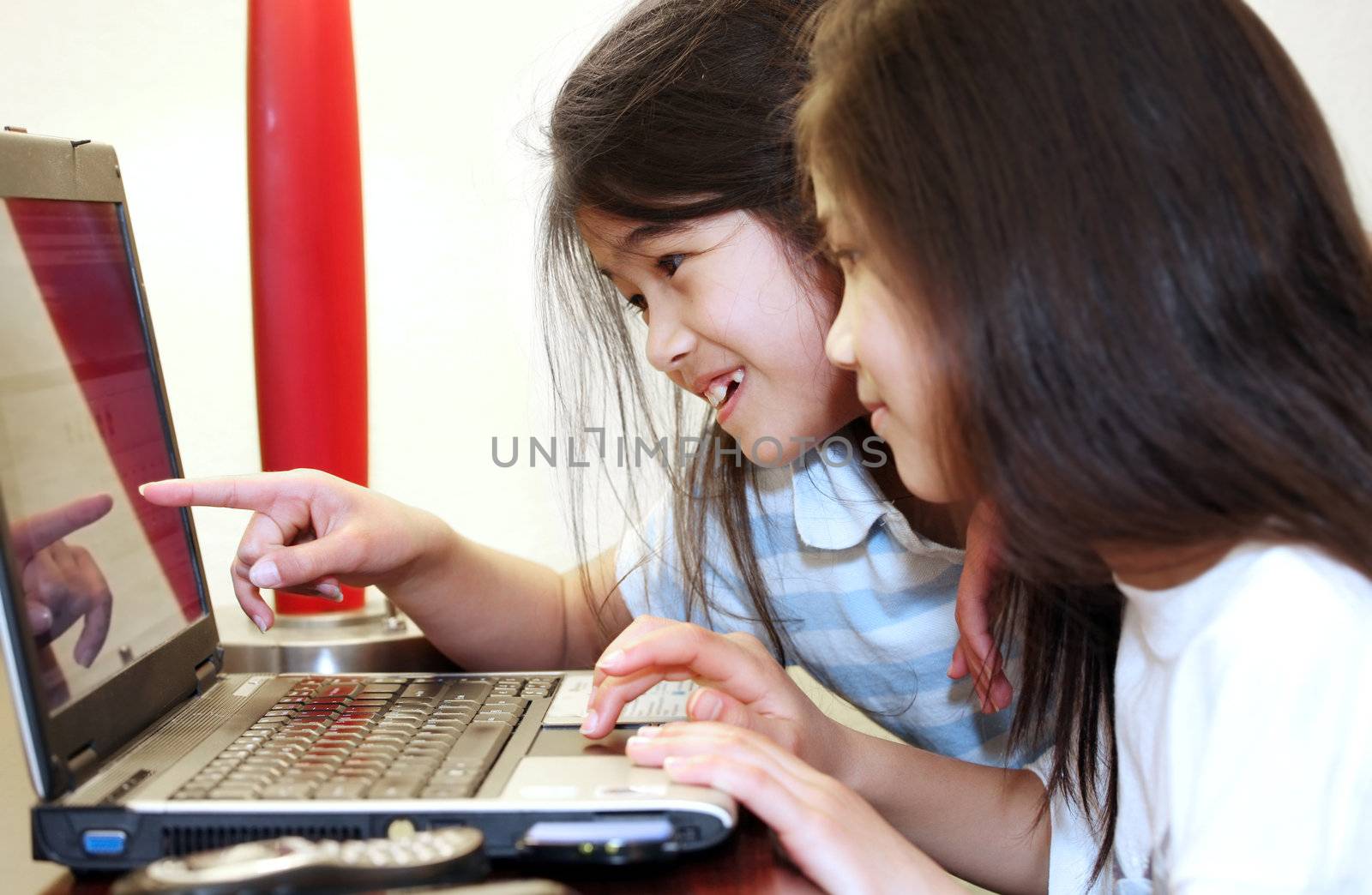 Two little girls working on a laptop  computer, pointing to screen