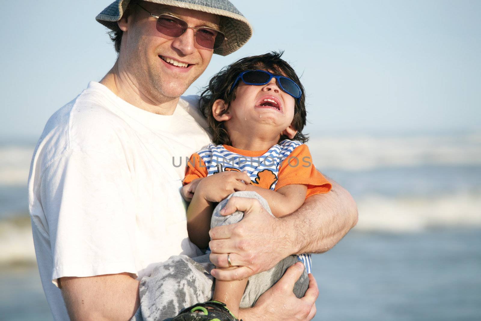 Father holding crying two year old child at beach