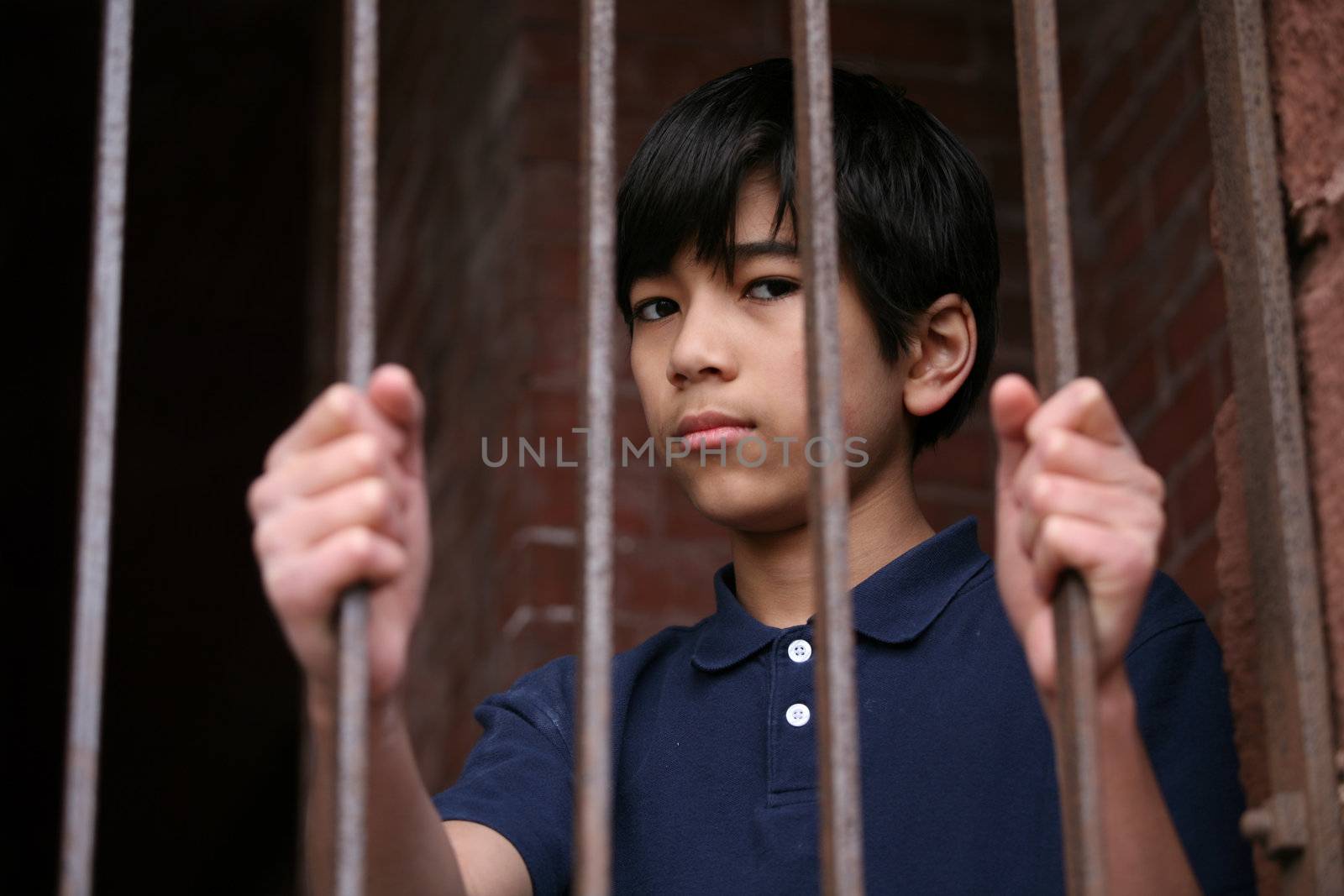 Boy standing behind bars, sad  or wary expression