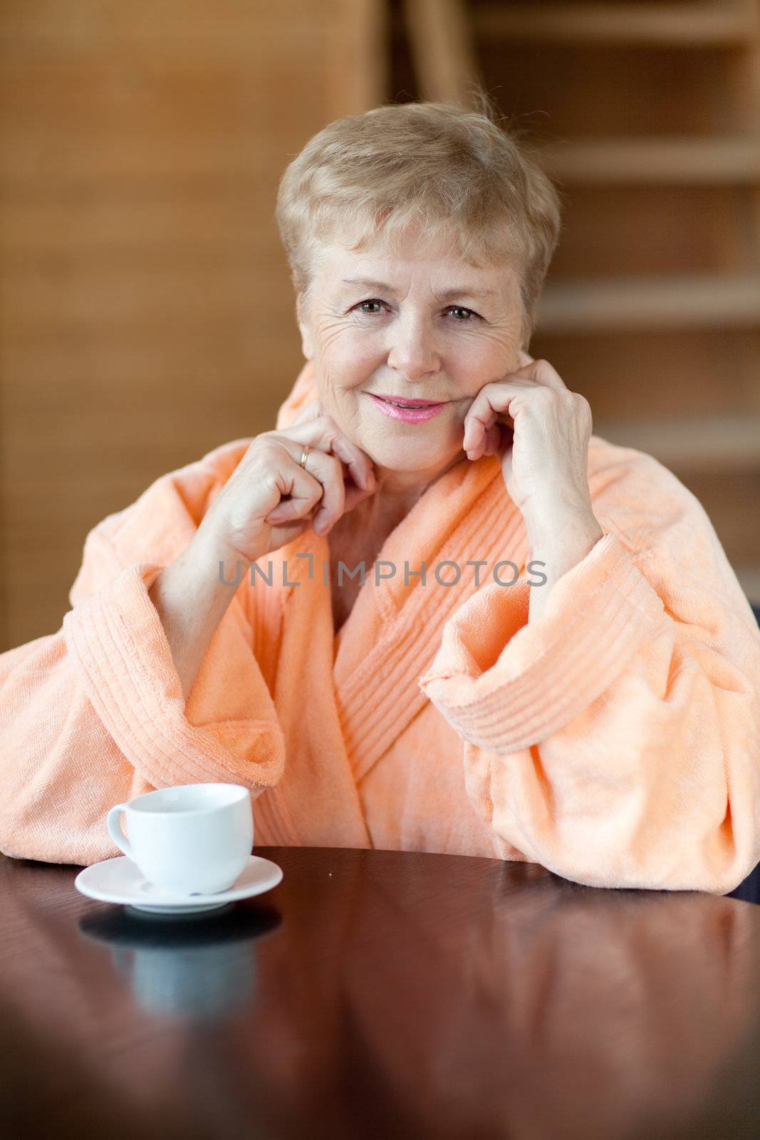 The elderly woman in a pink dressing gown looks in a camera