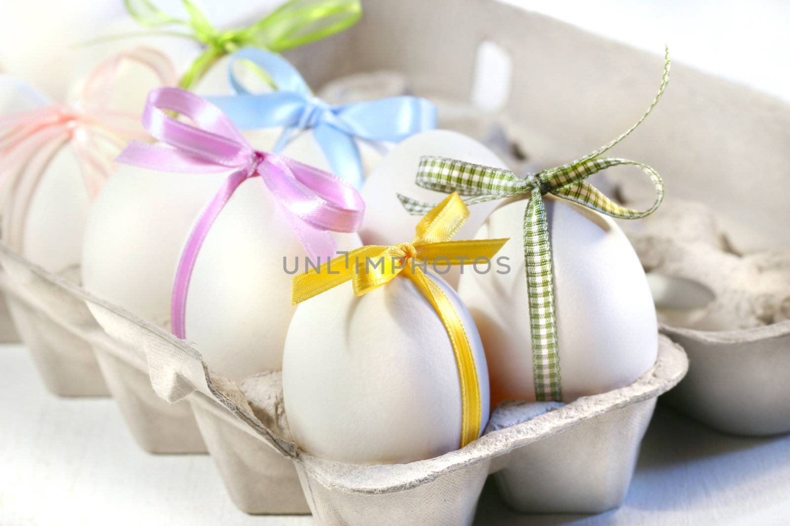 White eggs with colored ribbons in cardboard crate 