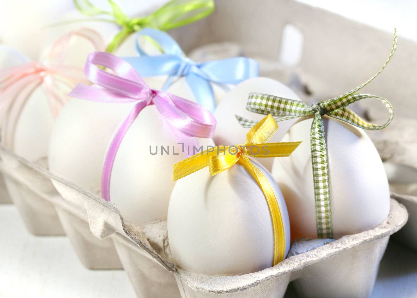 White eggs with colored ribbons in cardboard crate 