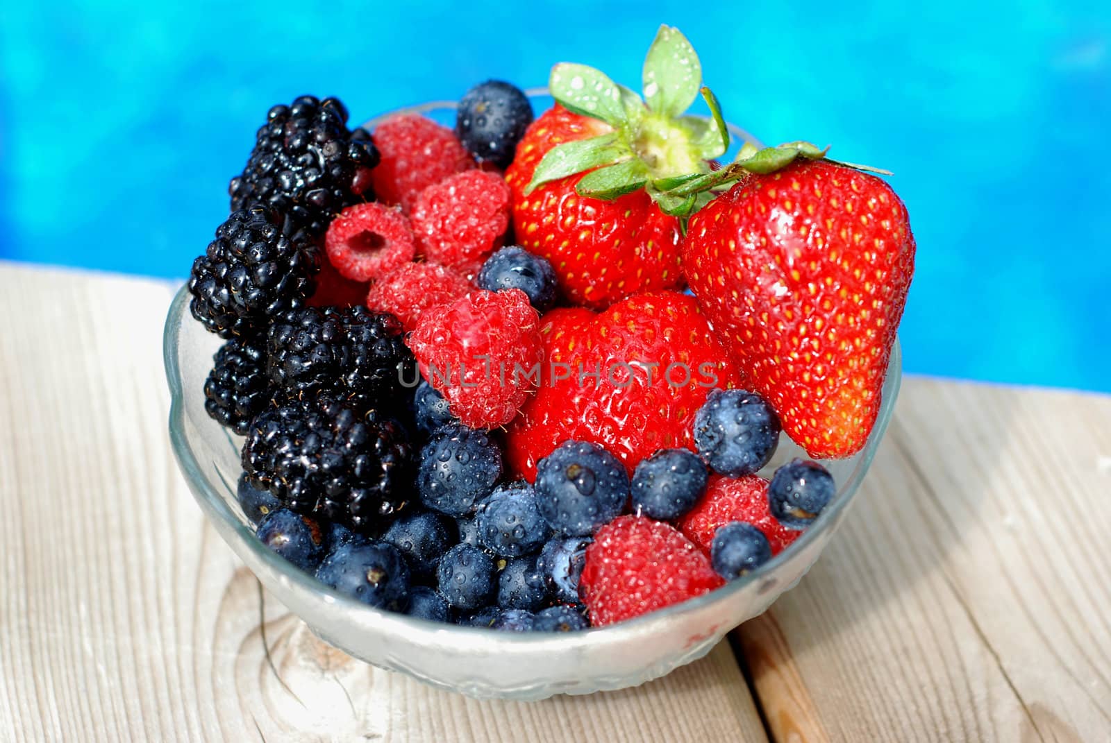 Bowl of mixed berries on a wooden deck near a pool