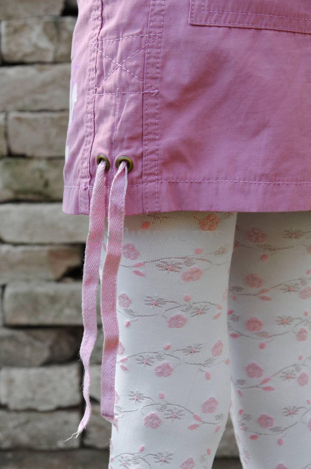 Fashion detail of female model wearing pink mini skirt and embroidered legwear with bricks in background