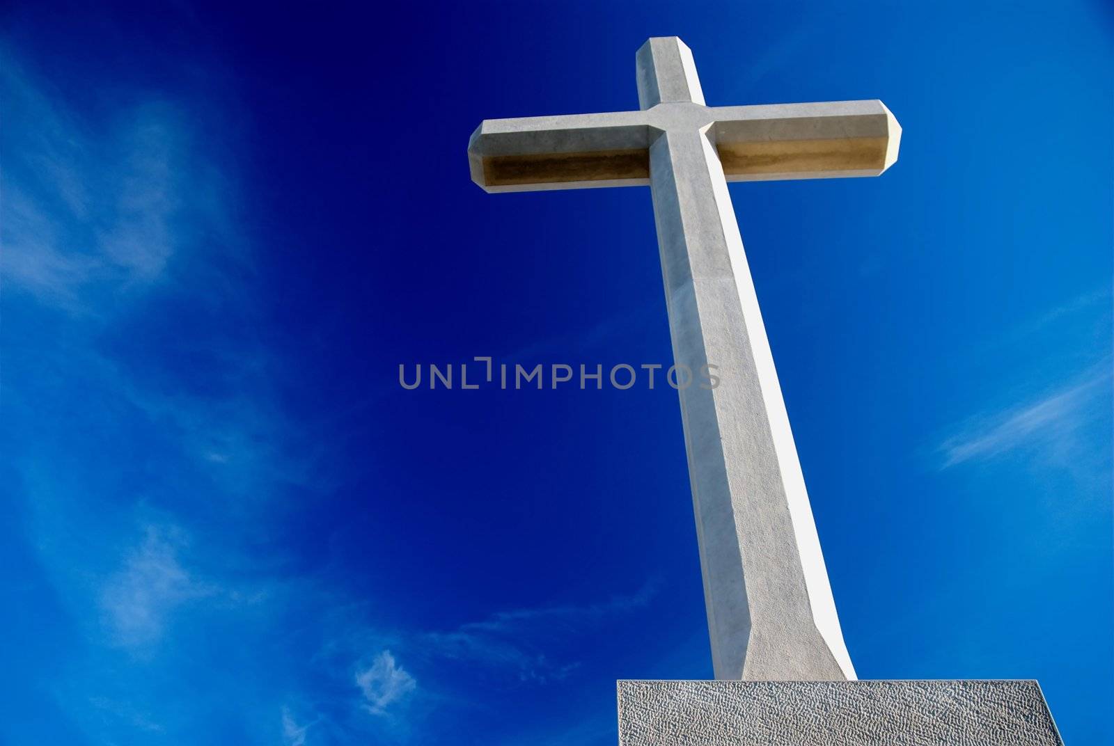 Big Christian stone cross over blue sky and clouds - dramatic bottom racurs