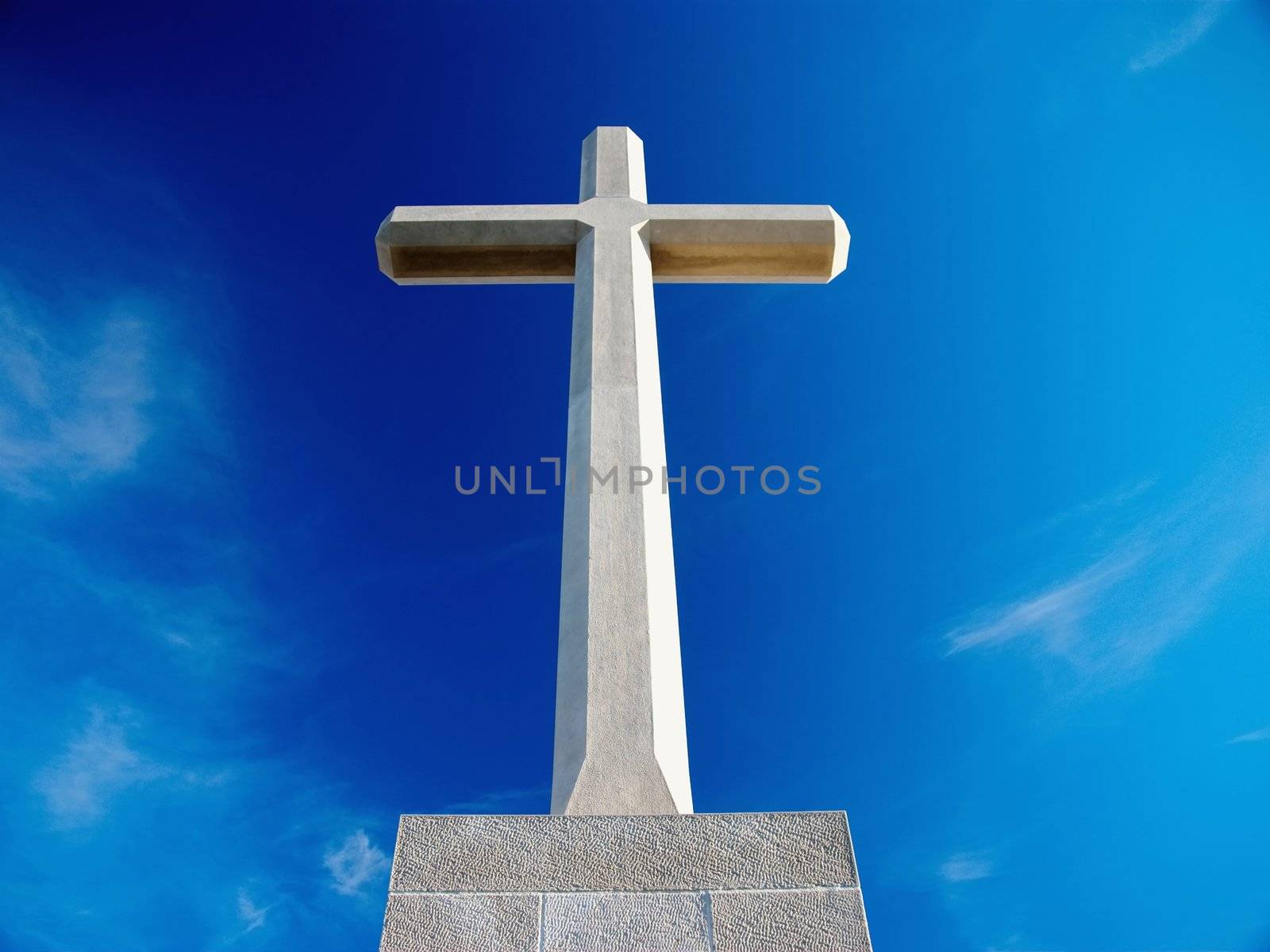 Big Christian stone cross over blue sky and clouds - bottom racurs