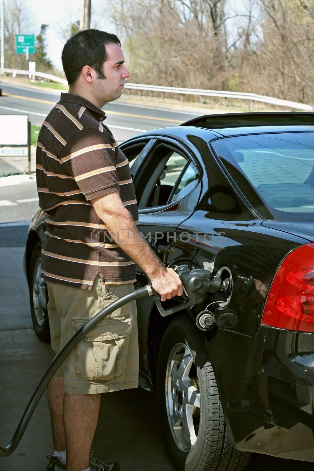 A man pumping high priced gas into his car with a disgusted look on his face.