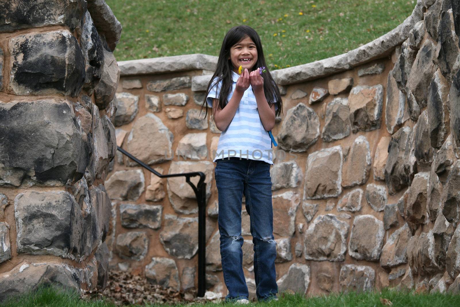 Happy little girl holding small flowers outdoors, standing between stone walls