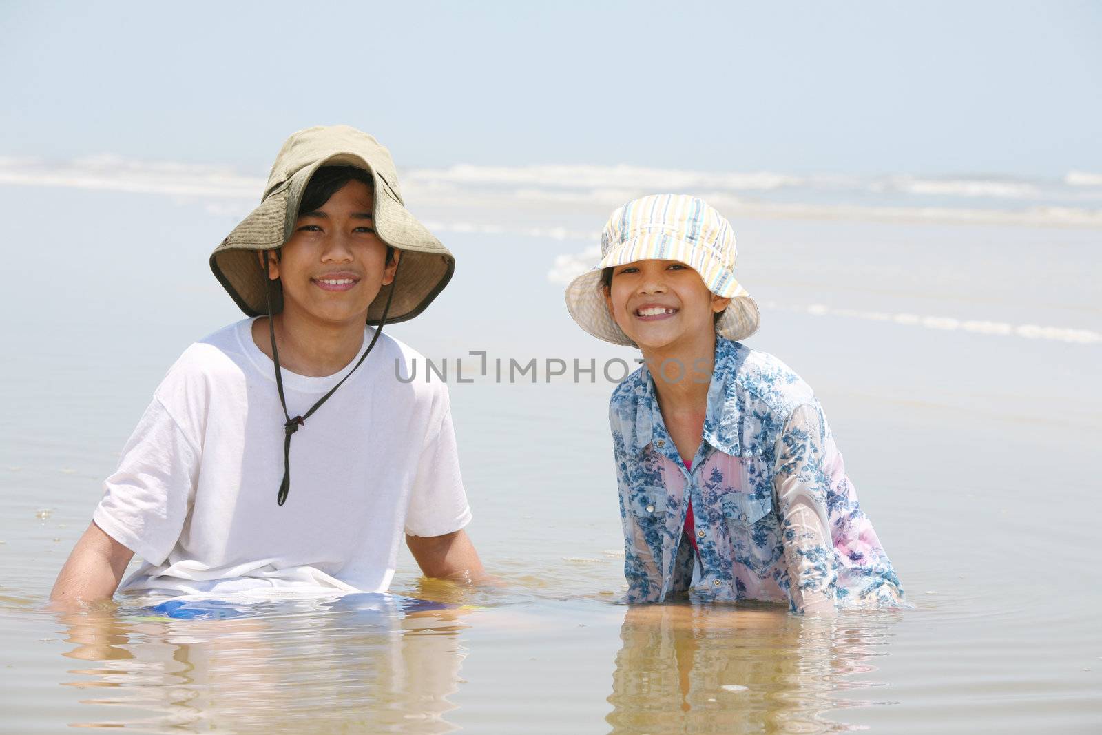 Two children sitting in water at ocean shore by jarenwicklund
