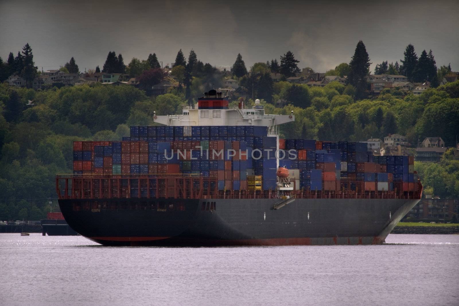 Stormy Container Ship with smoke or steam coming out of the top of the stack. Stormy skies from a typical Seattle Puget Sound day are evident. Logos have been obscurred or otherwise removed.