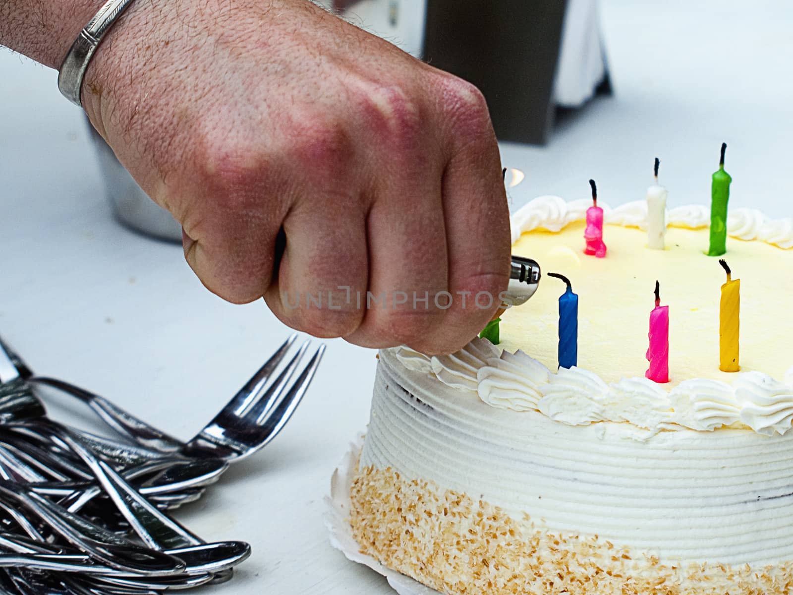 An adult male lighting the candles on a birthday cake.