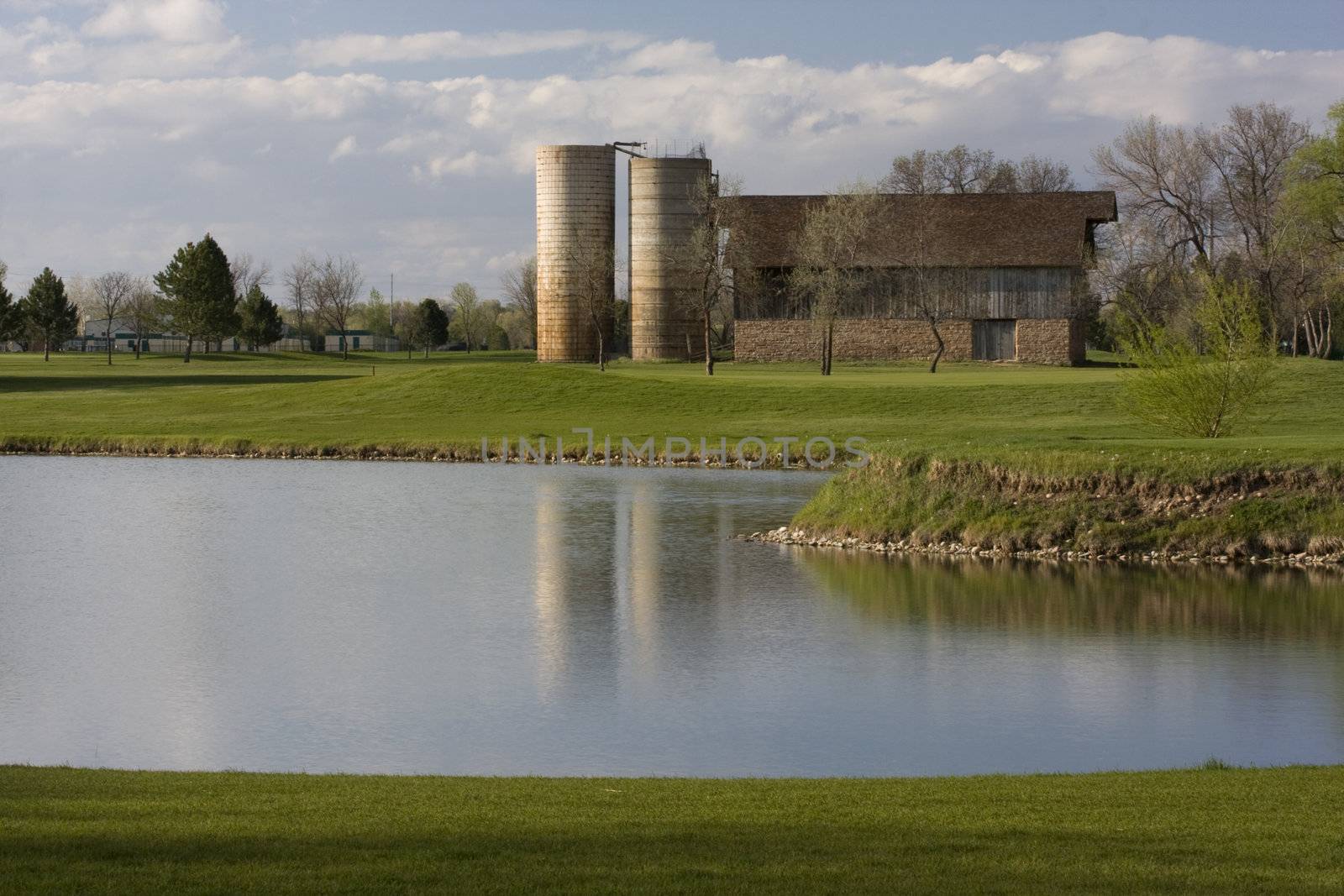 barn with two silos surrounded by green meadows, lake and houses - old farm turned into a golf course