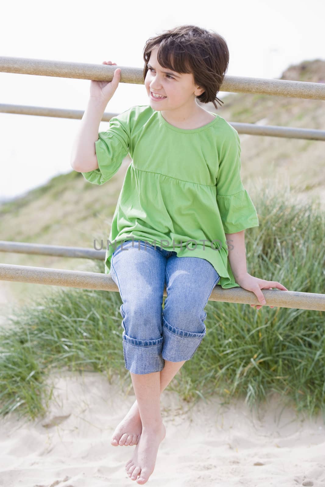 young child sitting on railings by the beach