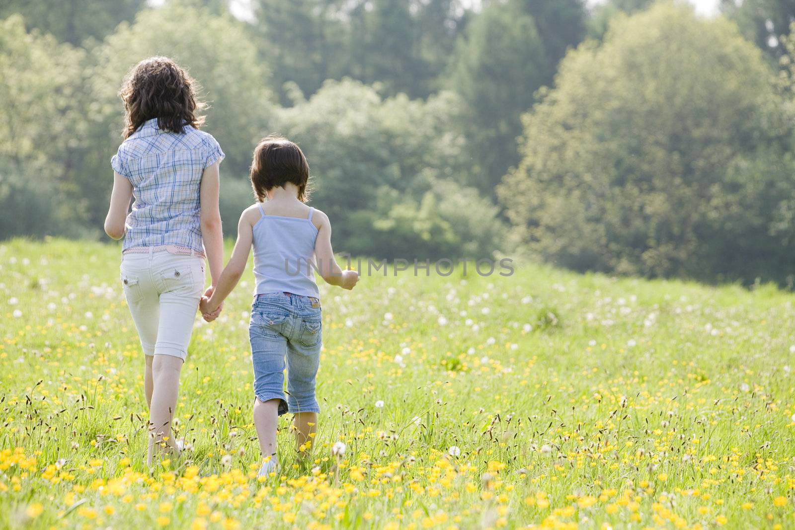 two girls walking away from camera in a field full of buttercups and dandelions with space for copy