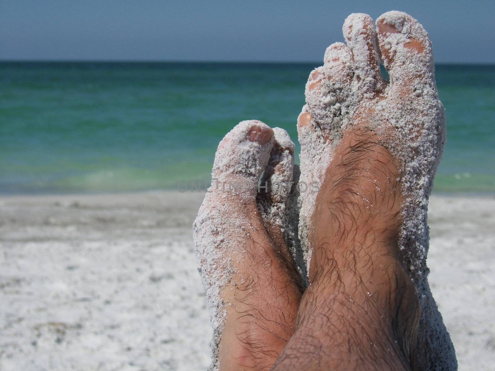  pair of feet crossed on a beach covered in sand