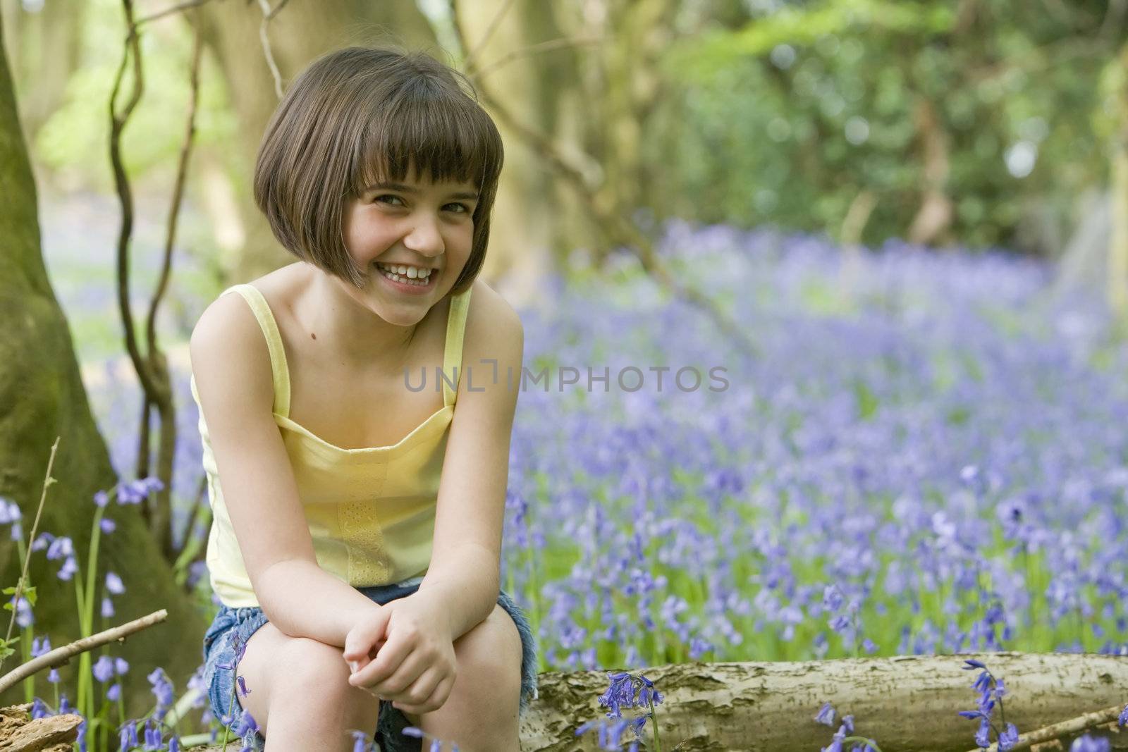 young female child sitting in a field of bluebells with space for copy