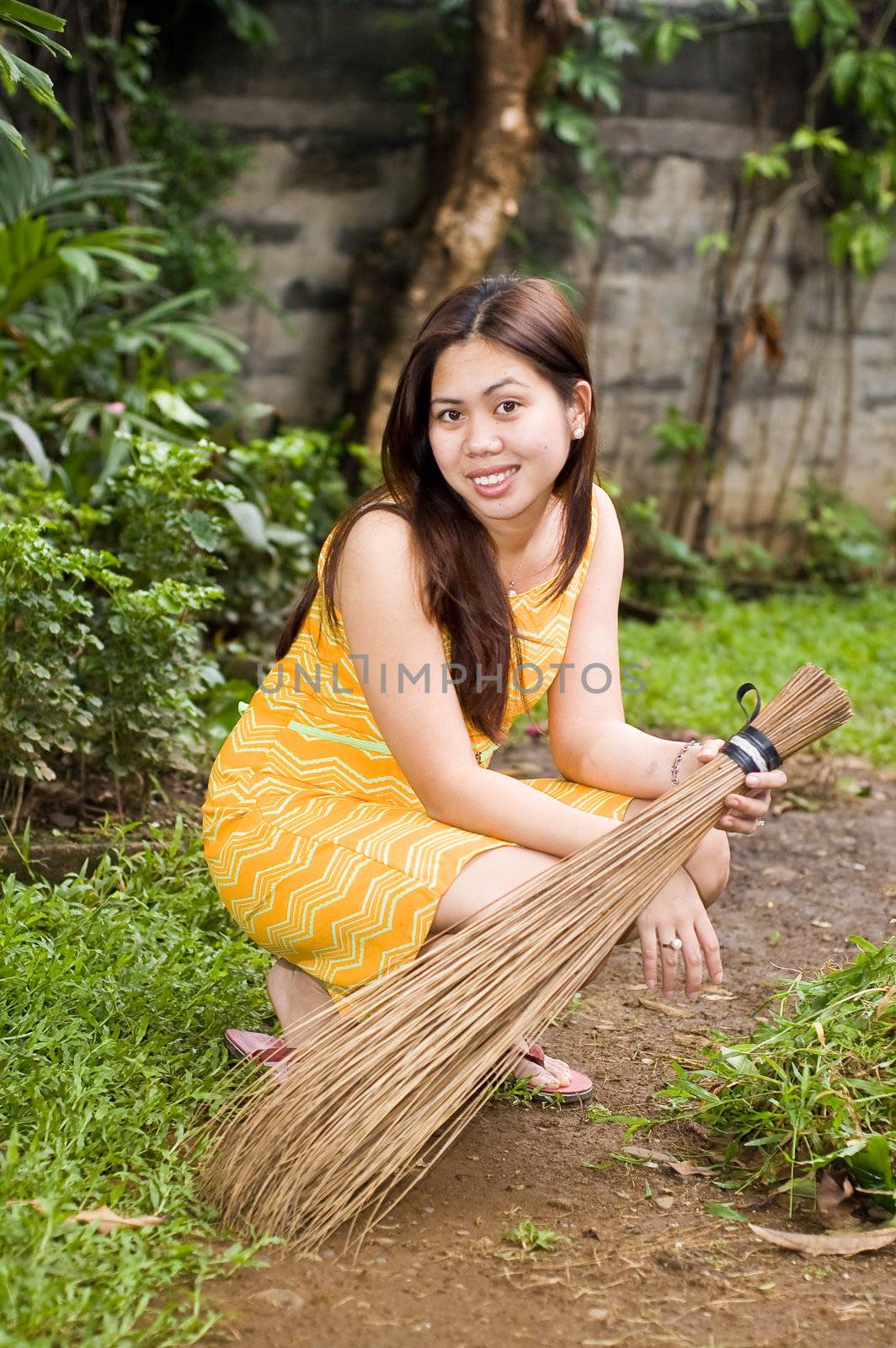 Gorgeous lady holding a broom crouched on garden