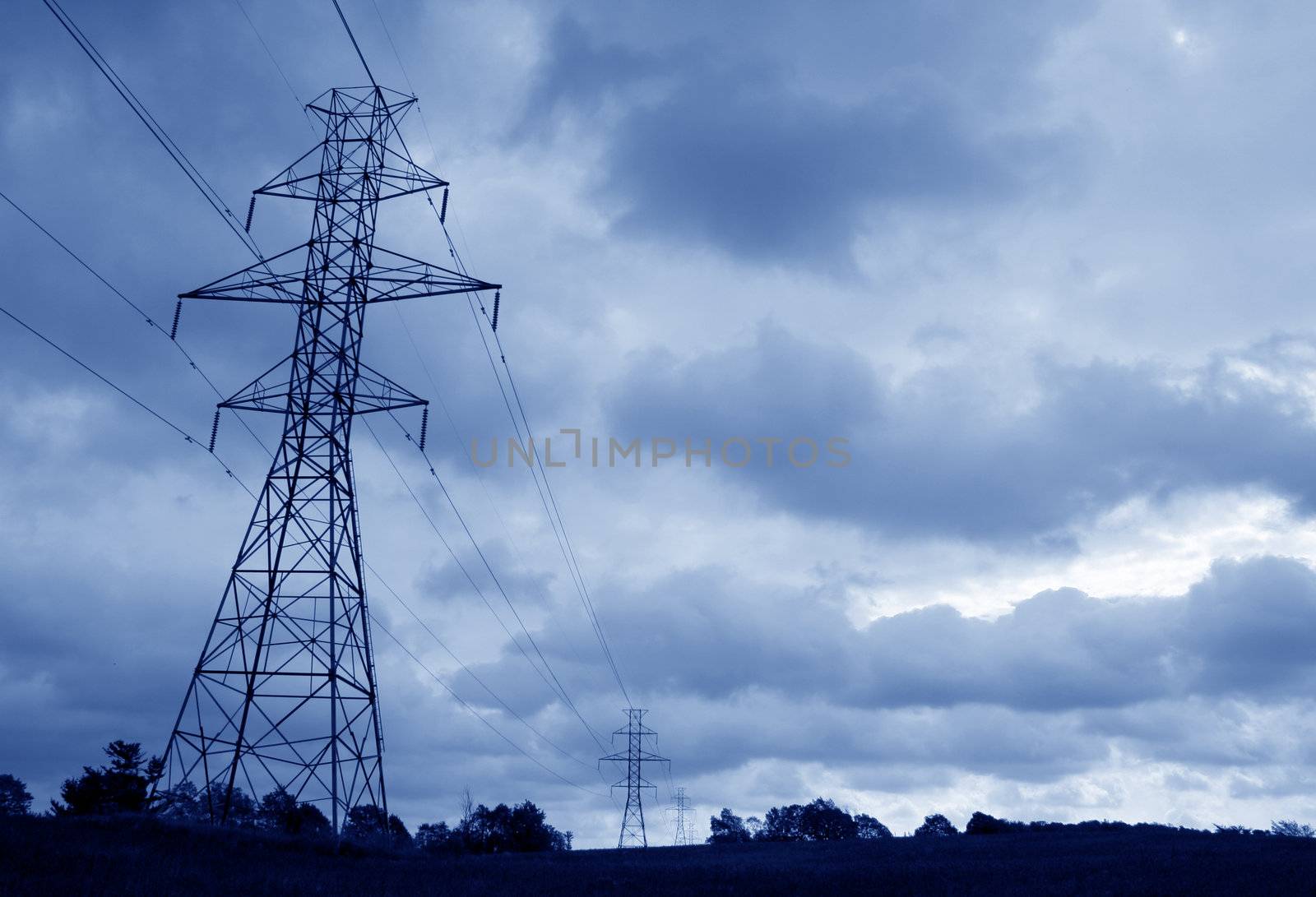 The silhouette of a power lines and towers against blue sky.

