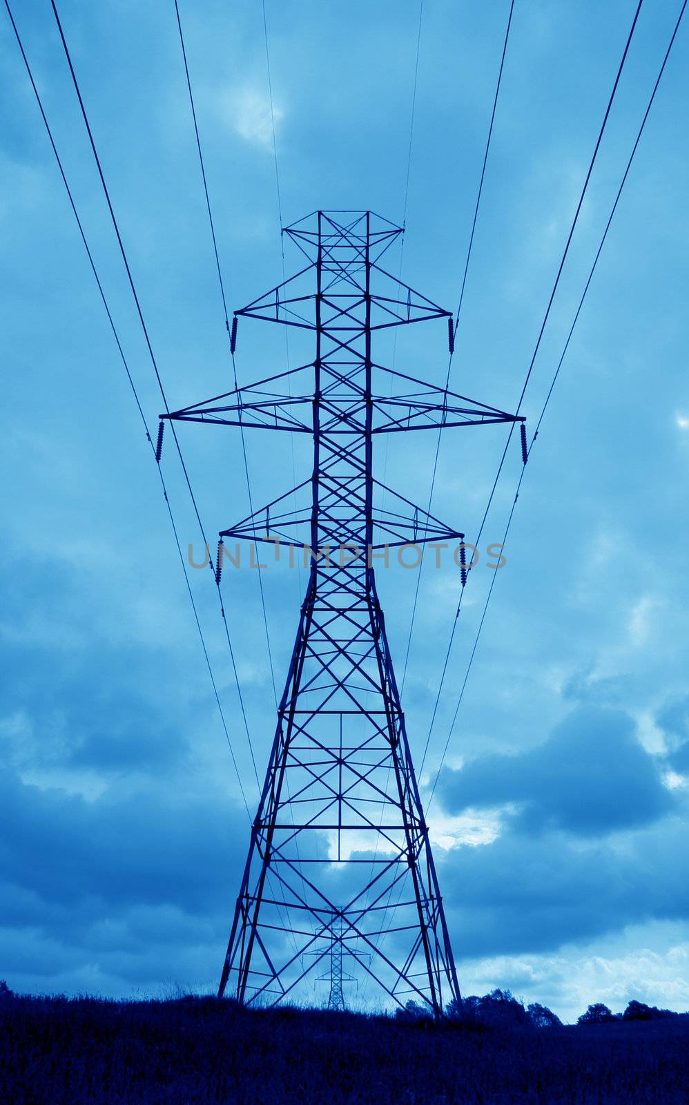 The silhouette of a power lines and towers against blue sky.
