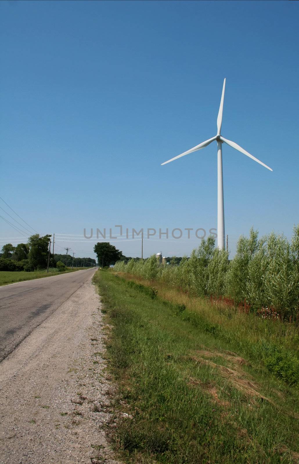 A windmill power generator on the side of the road in the middle of farm land.