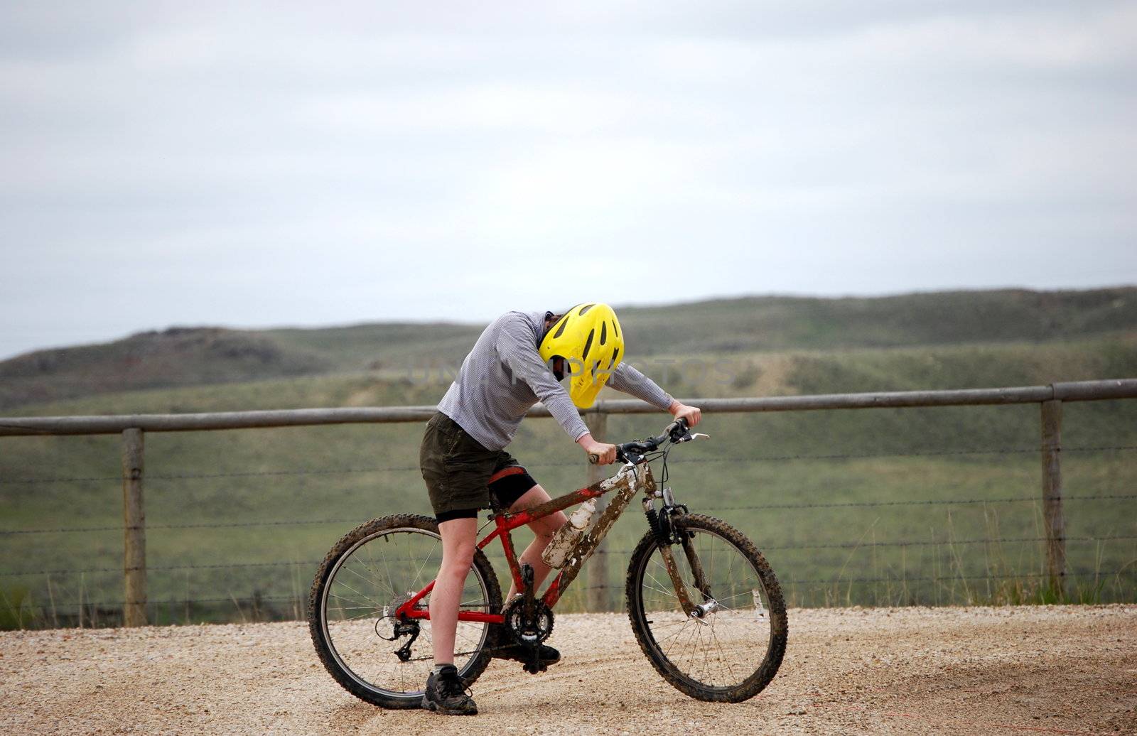 Mud-splattered mountain biker against a dirt road and green pasture.